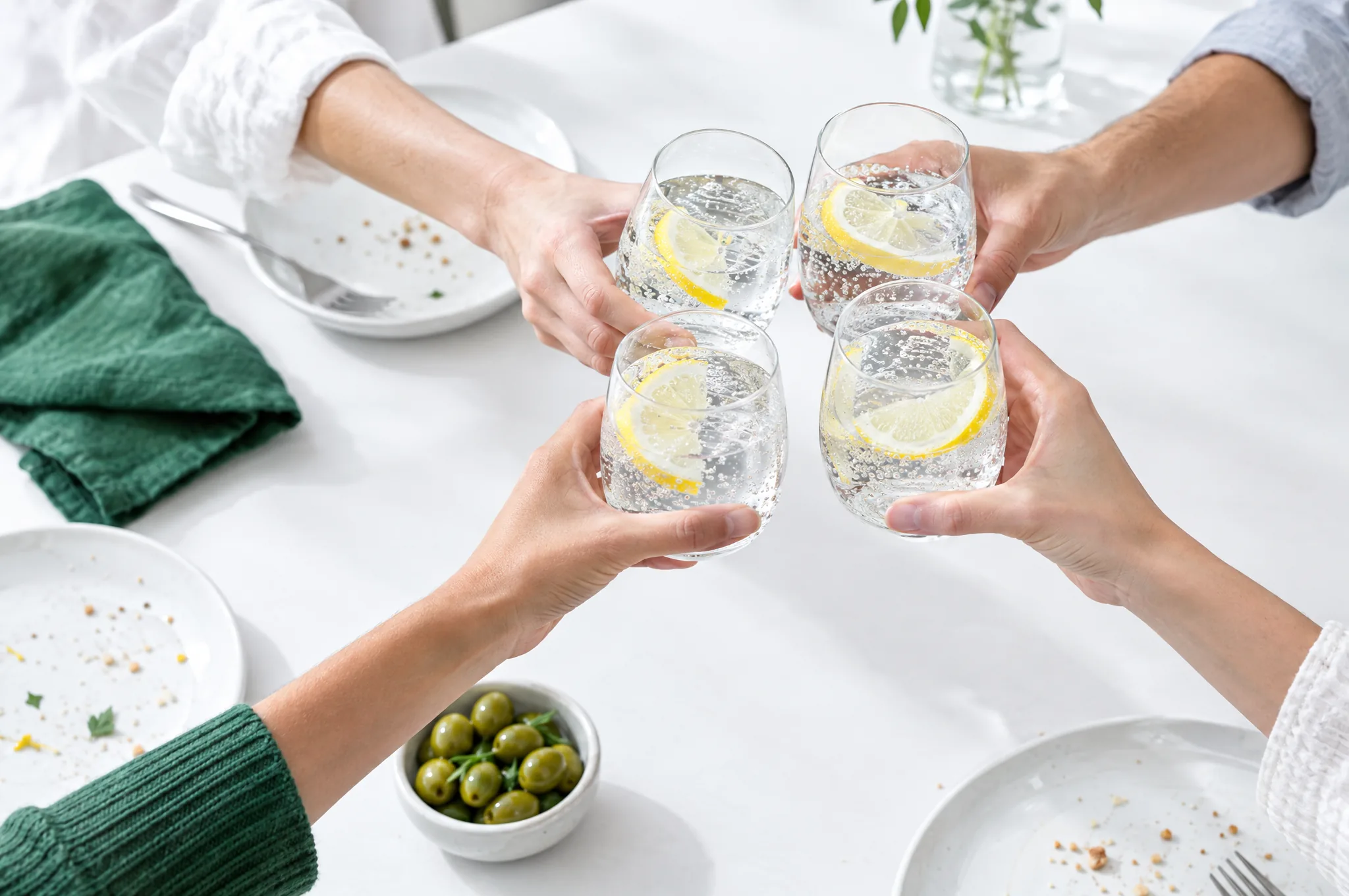 Quatre verres qui trinquent au-dessus d’une table, à la fin d’un repas.
